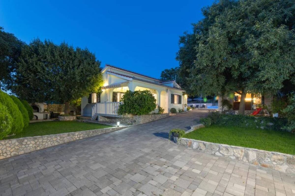 A two-story house with a paved driveway leading to a front door, surrounded by well-maintained lawns and trees.