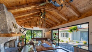 Un comedor amplio con mesa y bancos de madera, chimenea de piedra y vistas al jardín exterior.