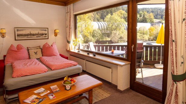 A cozy room with a bed, a table with magazines, a window with a view of trees, and a wooden ceiling. - Dachstein Top 12 by Interhome (Flachau)