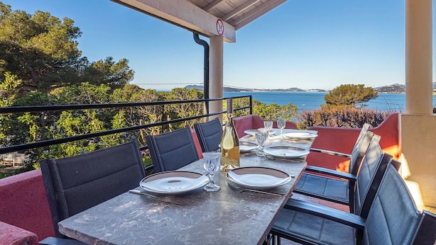 An outdoor dining area with a table set for two, overlooking a scenic view of the sea and hills. - Le Provençal by Interhome (Le Pradet)