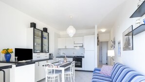 Una cocina moderna con armarios blancos, un comedor con mesa y sillas, y una sala de estar con un sofá a rayas.