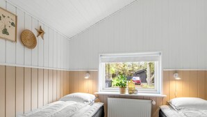 A room with two single beds, a window with a view of the outside, a radiator, and wall-mounted lamps.