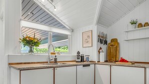 A kitchen with white cabinetry, a window with a view, a coffee machine, and a wooden cutting board with tomatoes.