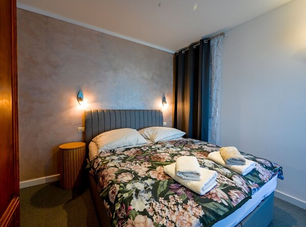 Una habitación de hotel con una cama, dos lámparas de pared, una mesita redonda y una cortina.