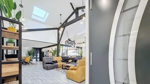 Ein modernes Wohnzimmer mit einer Couch, Sesseln und einem Couchtisch. Ein Fahrrad hängt an der Wand und eine Pflanze steht auf einem Regal.