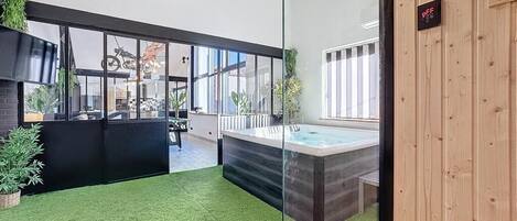 Un espace intérieur moderne doté d’une paroi en verre, d’un jacuzzi et d’un mur en bois sur lequel est fixé un panneau.