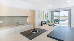 Eine moderne Küche mit Einbauherd, ein Essbereich mit einem schwarzen Tisch und Blick auf einen Swimmingpool durch große Fenster.