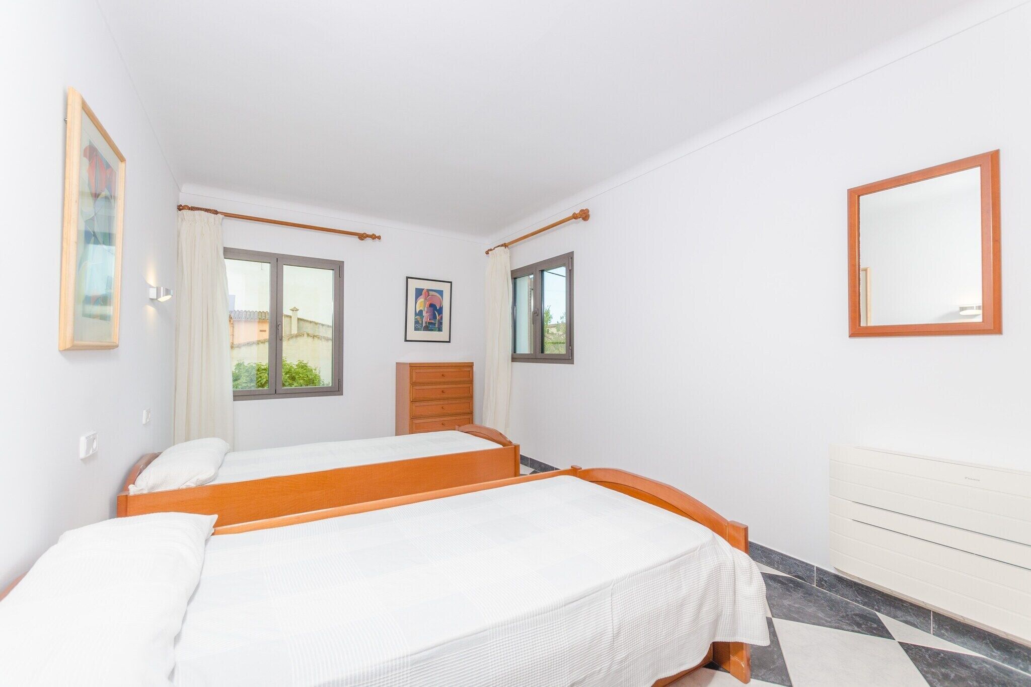 A bedroom with two beds, a dresser, a window with curtains, and a mirror on the wall.