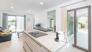 Eine moderne Küche mit einer zentralen Kochinsel, einem Essbereich mit einer Couch und einer Glastür zum Außenbereich.