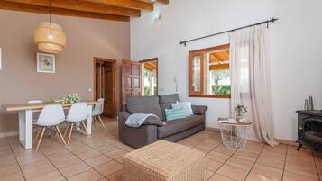 A cozy living room with a sofa, dining table, chairs, and a wicker ottoman.