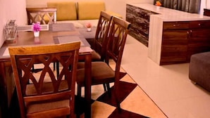 A dining area with a table and chairs, a sofa, a ceiling fan, and a painting on the wall. - Kivi stays  (Pune)