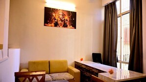 A living room with a yellow sofa, a dining table, and a painting of a deity on the wall. - Kivi stays  (Pune)