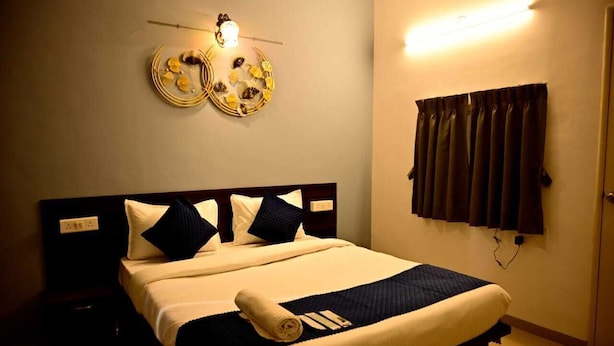 A neatly made bed with a dark headboard, a wall-mounted light fixture, and a window with curtains. - Kivi stays  (Pune)