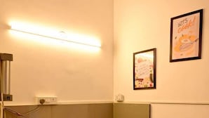 A small bathroom with a dark wooden vanity, a mirror, and a wall-mounted light fixture. - Kivi stays  (Pune)