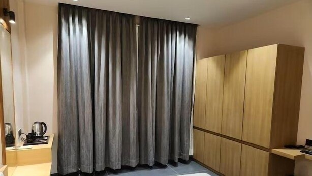 A hotel room with a bed, a wardrobe, a nightstand with a kettle, and a window with curtains.