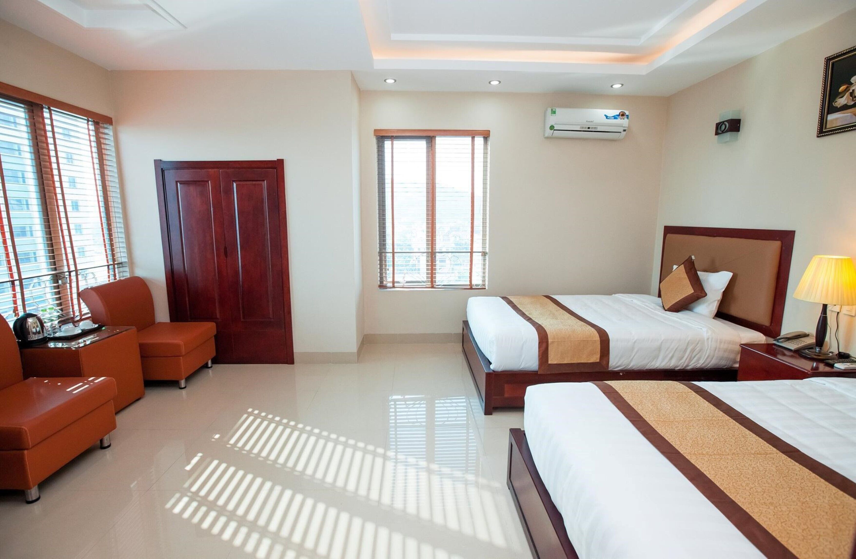 A hotel room with two beds, a desk, a chair, a wardrobe, and a window.