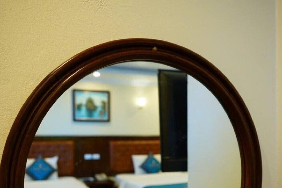 A round mirror reflecting a hotel room with two beds, a wooden headboard, and a painting on the wall.