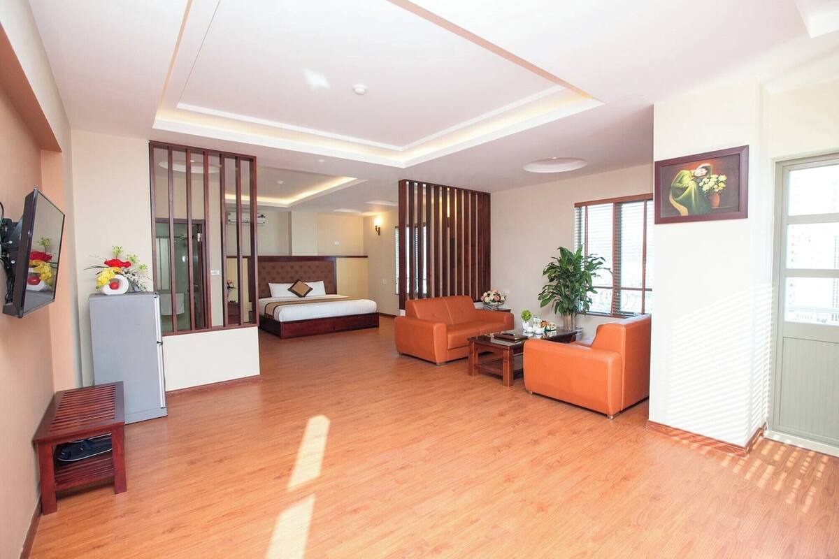 A hotel room with a bed, a sofa, a small table, a TV, and a potted plant.