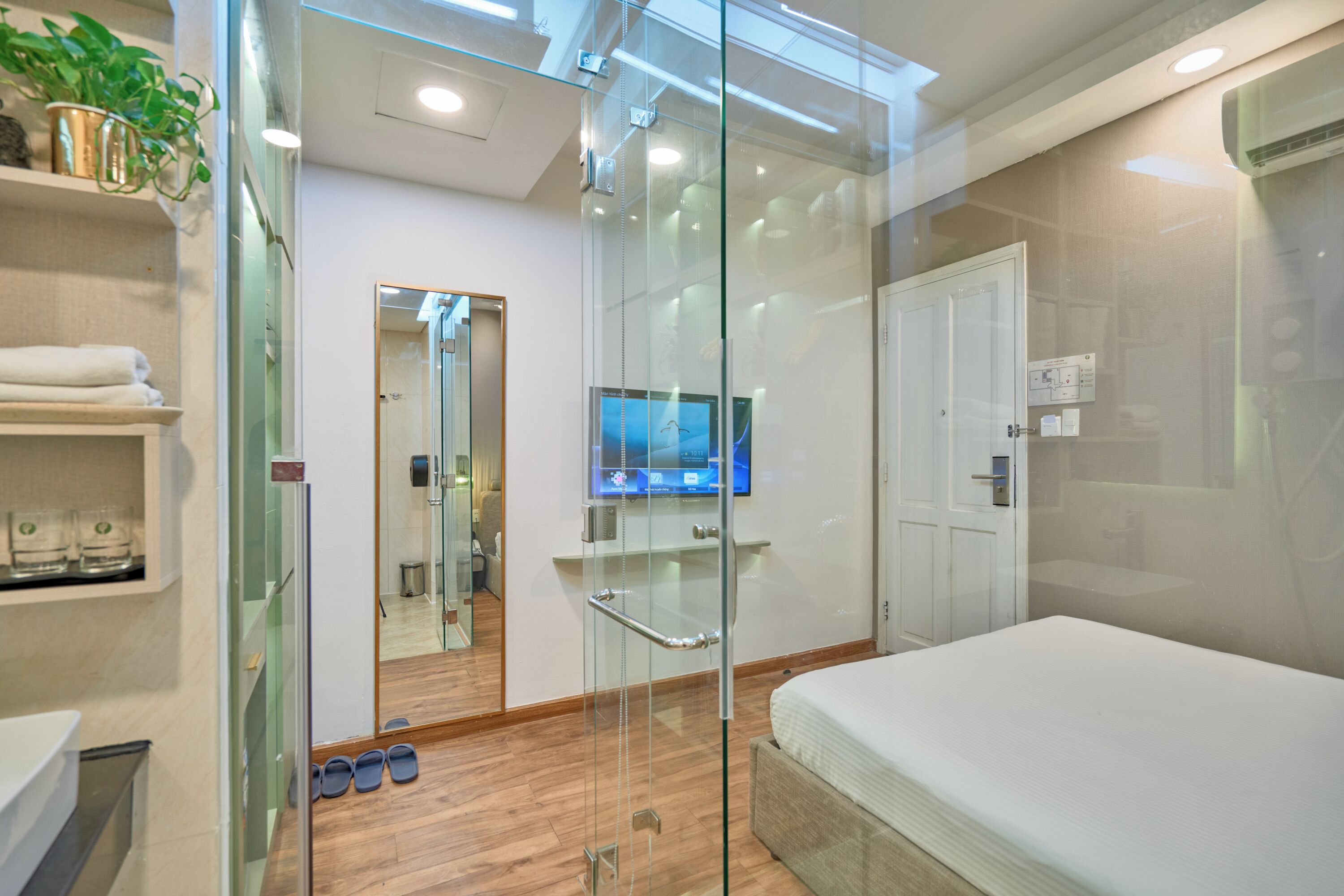 A modern hotel room with a glass partition, a bed, a television, and a shower area.