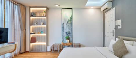 Una habitación de hotel con cama, televisión, escritorio, estantería y un amplio ventanal con cortinas.