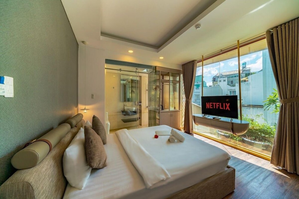 Quarto de hotel com cama, televisão exibindo Netflix e vista para o exterior.