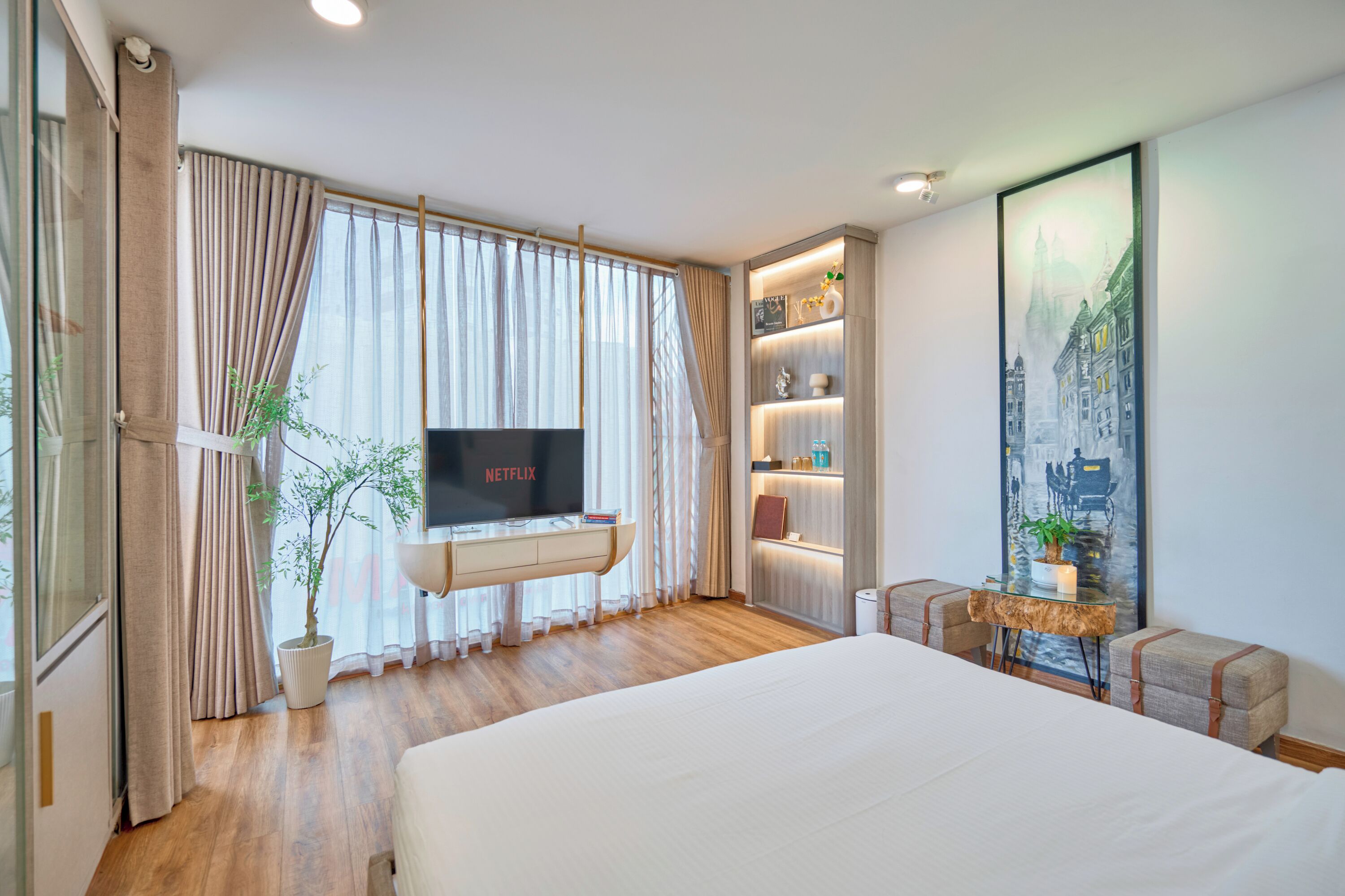 Una habitación de hotel moderna con una cama grande, un televisor, una planta y una estantería.