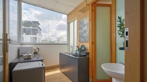 A compact kitchen with a refrigerator, stove, and sink, a small dining area, and a view of the cityscape through large windows.