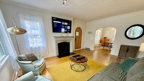 A living room with a fireplace, a TV mounted on the wall, and a dining area in the background.
