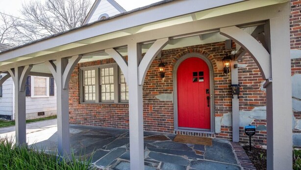 A house with a red door, brick exterior, and a covered porch with white columns.