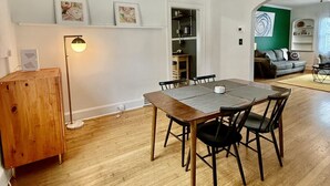 A dining area with a wooden table and chairs, a pendant light, and a view into the kitchen.