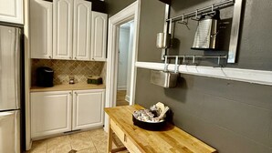 A kitchen with white cabinets, a wooden table, and a metal rack with kitchen utensils.