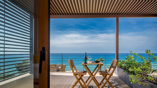 A balcony with a wooden table and chairs, overlooking a clear blue sea.