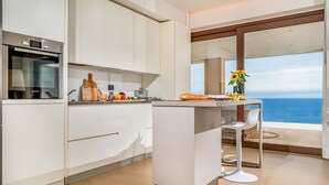 A modern kitchen with a built-in oven, a central island with seating, and a view of the ocean.