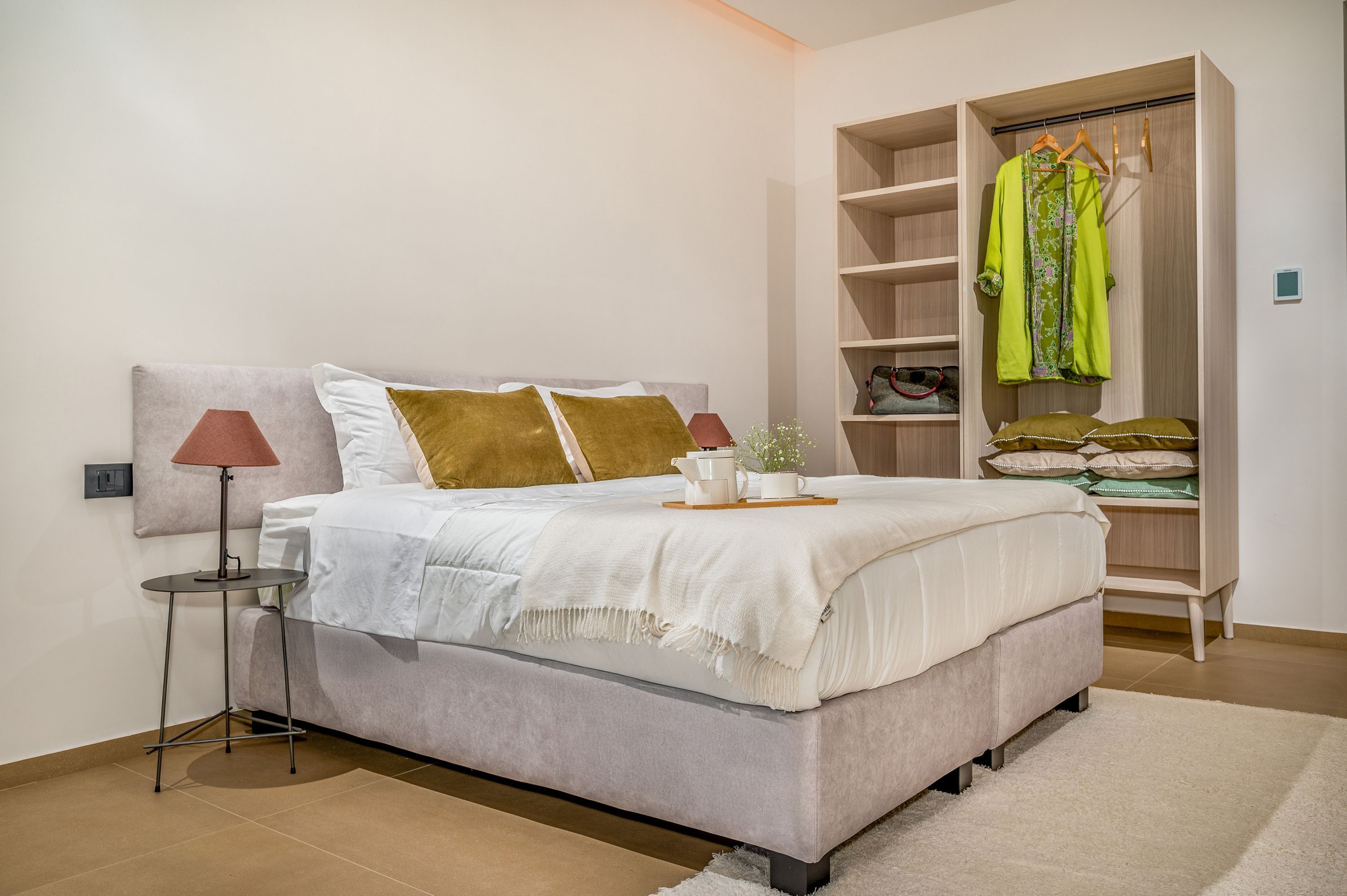 A modern bedroom with a bed, bedside table, lamp, and a wardrobe with clothes hanging inside.