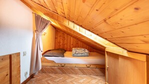 Une petite chambre mansardée en bois, avec un lit simple, une fenêtre avec des rideaux et un parquet à motifs en chevrons.