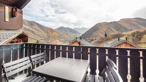 Un balcon doté d’une table en bois et de bancs, offrant une vue sur une vallée bordée de montagnes et de maisons.