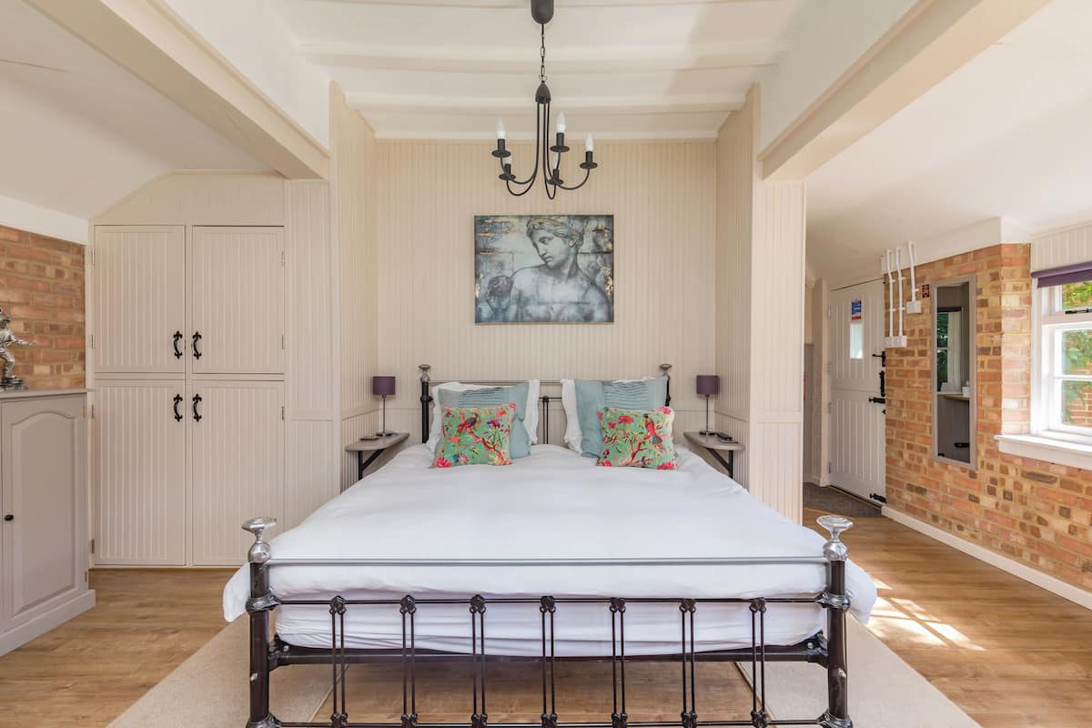 A bedroom with a large bed, a chandelier, a painting on the wall, and a brick wall.