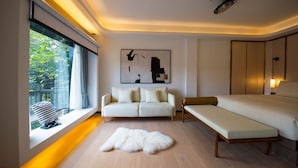 A modern hotel room with a large bed, a sofa, a bench, a fur rug, and a window with a view of greenery. - Xishangyunjian (Hangzhou)