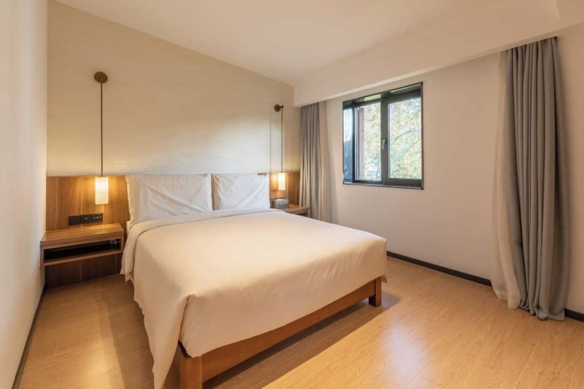 Ein modernes Schlafzimmer mit einem großen Bett, Nachttischlampen, einem Beistelltisch und einem Fenster mit Vorhängen.