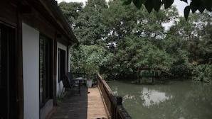 A wooden deck with a table and chairs, overlooking a calm body of water and dense greenery. - Xishangyunjian (Hangzhou)