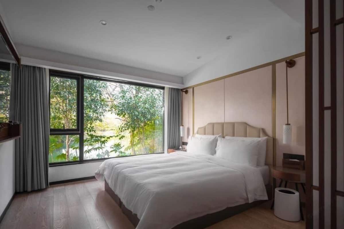 Ein modernes Hotelzimmer mit einem großen Bett, Blick auf Grün hinter einer Schiebetür und minimalistischem Design.