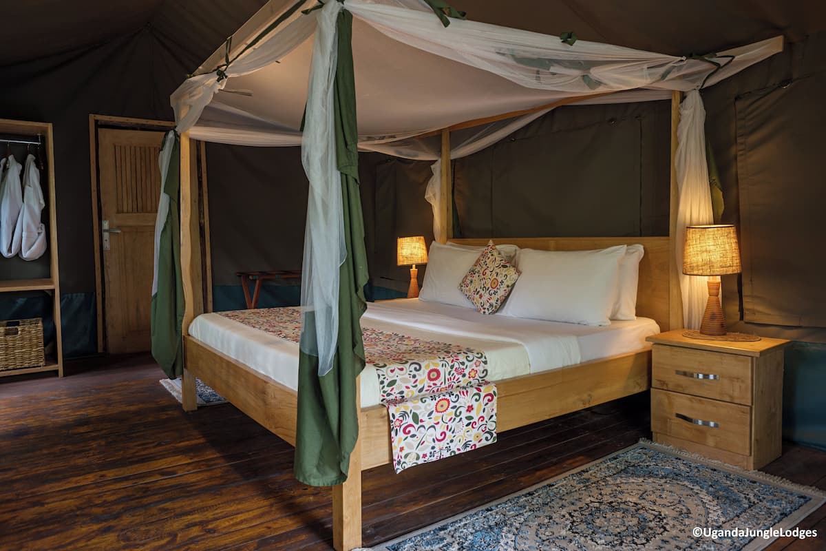 A tented room with a wooden bed, two bedside lamps, and a small wooden nightstand.