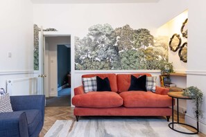 Relax in this inviting living room with a vibrant sofa, a mural of trees, and a cozy armchair.