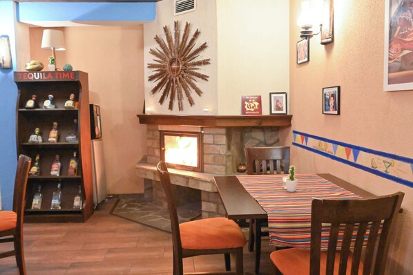 A cozy restaurant interior with a fireplace, wooden chairs, a striped tablecloth, and a tequila-themed shelf. - Chalet & Hotel IDA (Bansko)