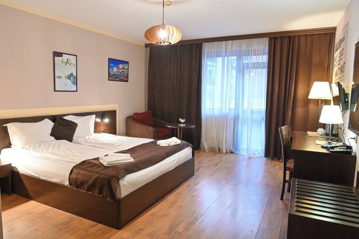 Ein Hotelzimmer mit einem großen Bett, einem Schreibtisch mit Lampe, einem Sessel und einem kleinen Tisch.