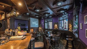 A bar area with wooden furniture, a projection screen displaying 'Dann's Bar', and a stone floor. - Chalet & Hotel IDA (Bansko)