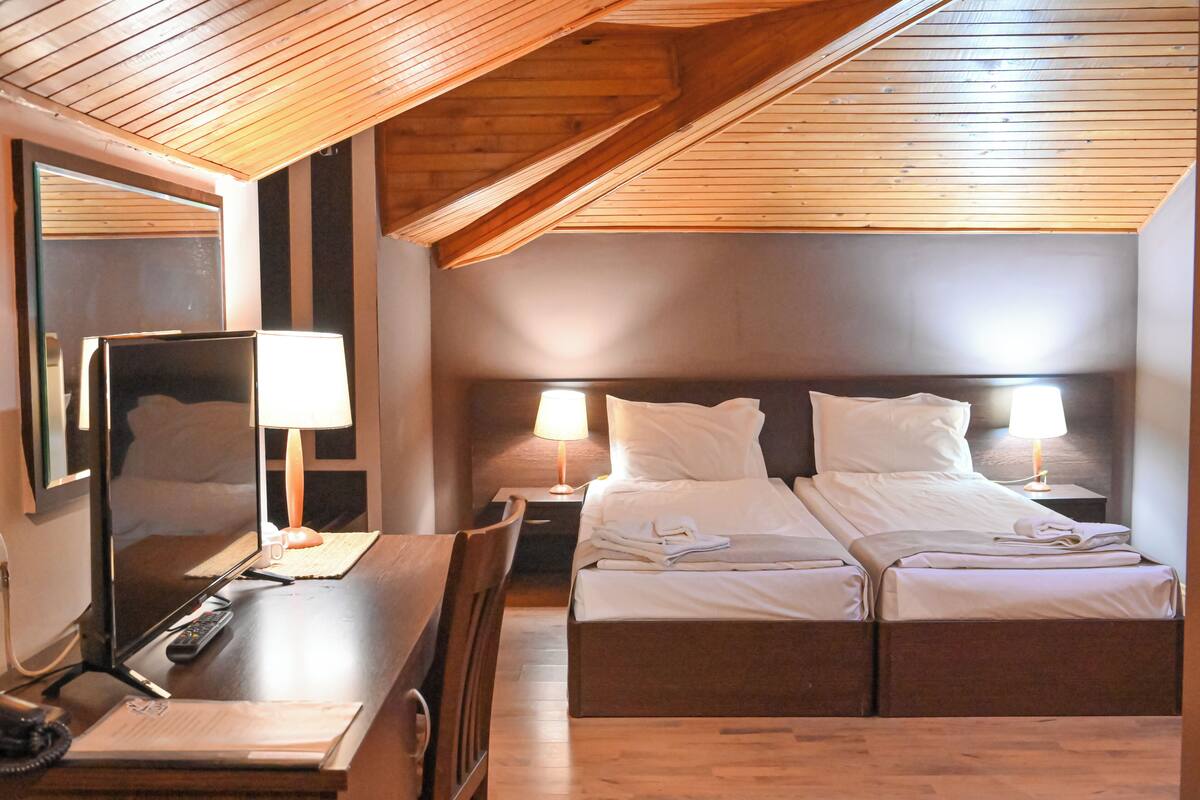 Ein Hotelzimmer mit Holzboden, einem Schreibtisch mit Lampe, einem Bett mit zwei Kissen und einem Nachttisch mit Lampe.