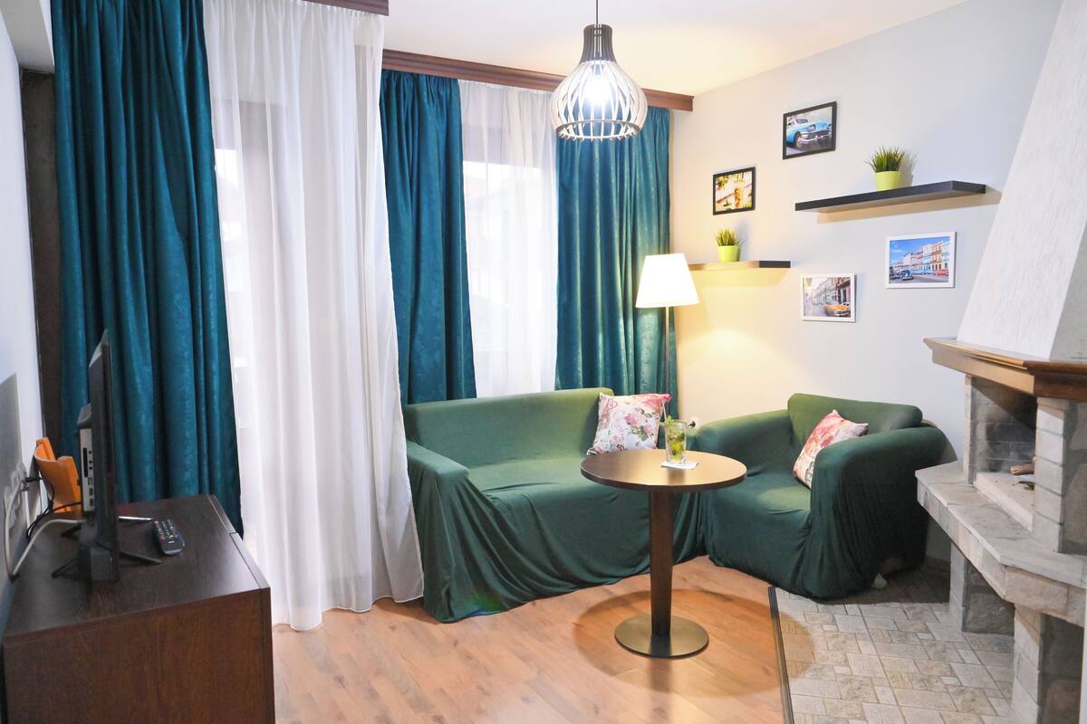 Ein gemütliches Zimmer mit einem grünen Sofa, einem kleinen runden Tisch, einer Lampe und einem Kamin.