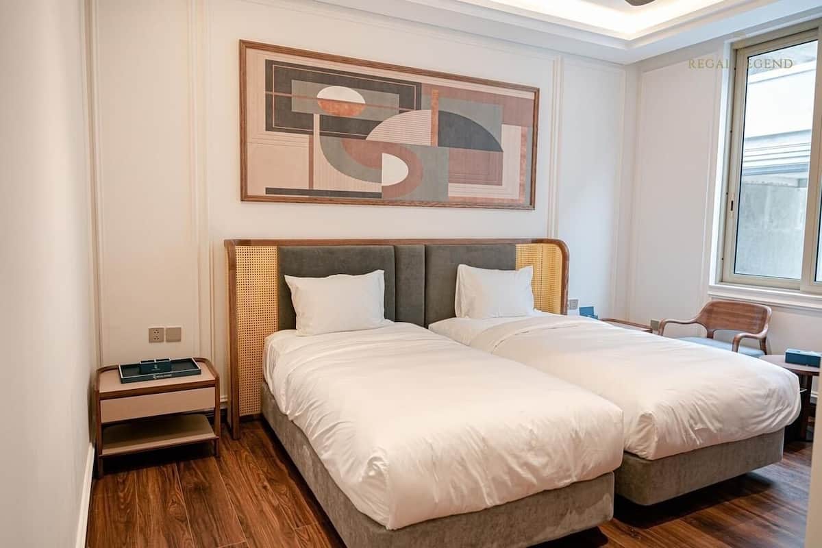 Ein Hotelzimmer mit zwei Betten, einem großen abstrakten Gemälde, einem Fenster und Holzboden.