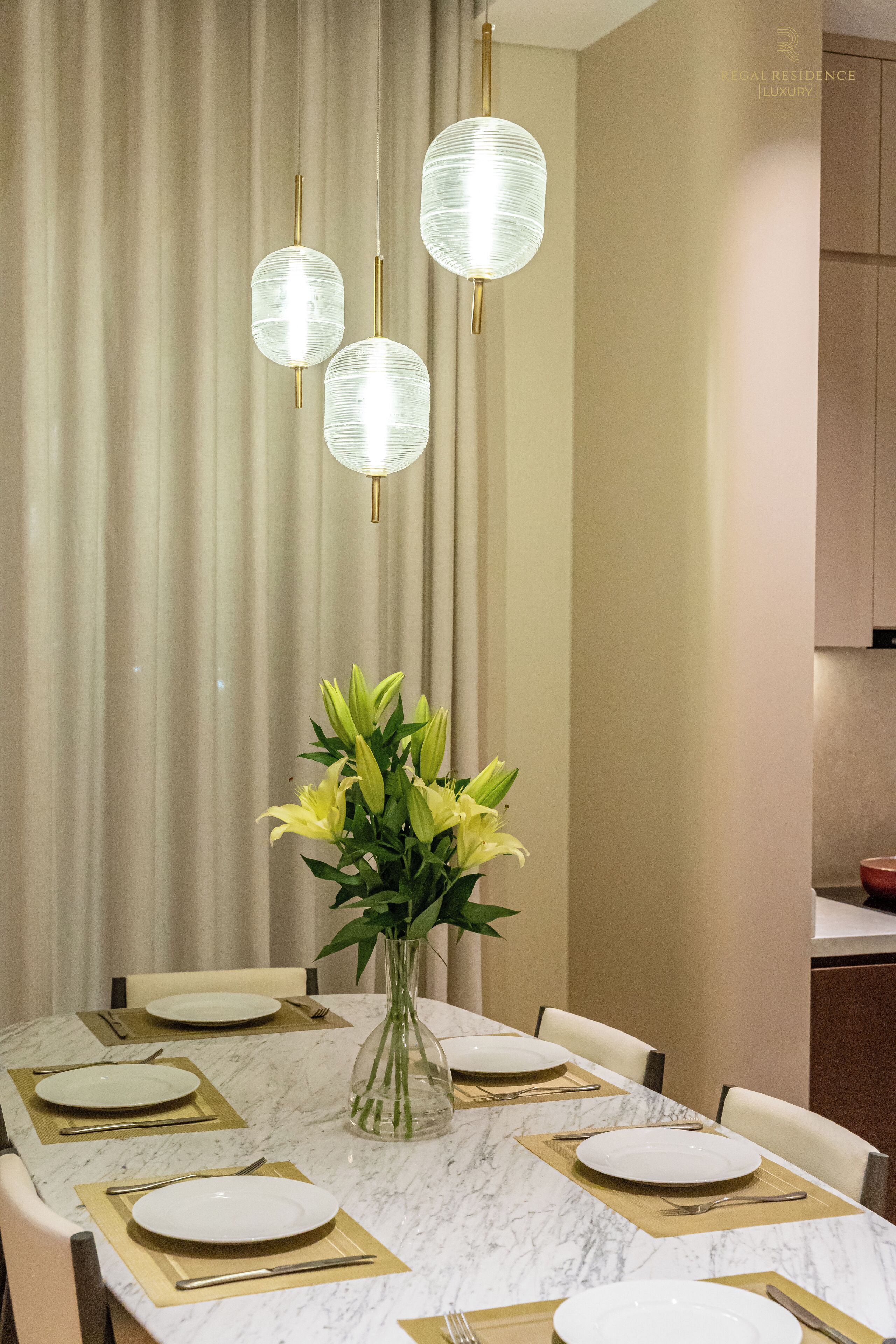 Comedor con una mesa de mármol, individuales dorados y un jarrón con flores amarillas.